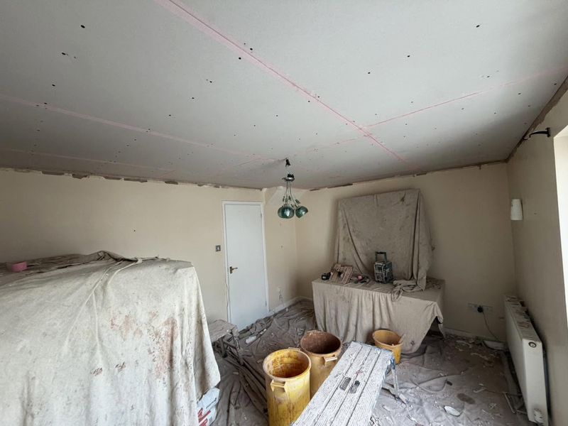 The same living room with the ceiling over-boarded and taped, furniture covered