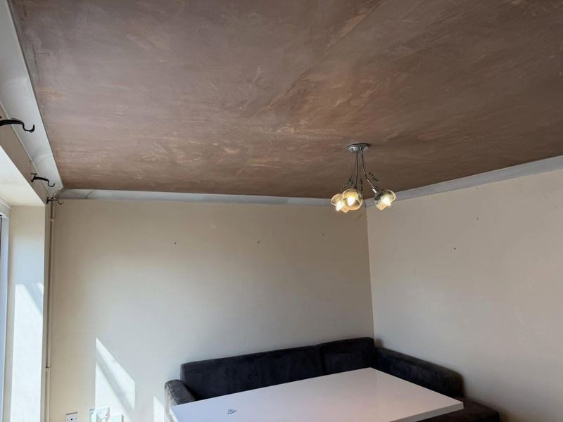 A living room ceiling skimmed in fresh plaster with new white coving and a light fitting
